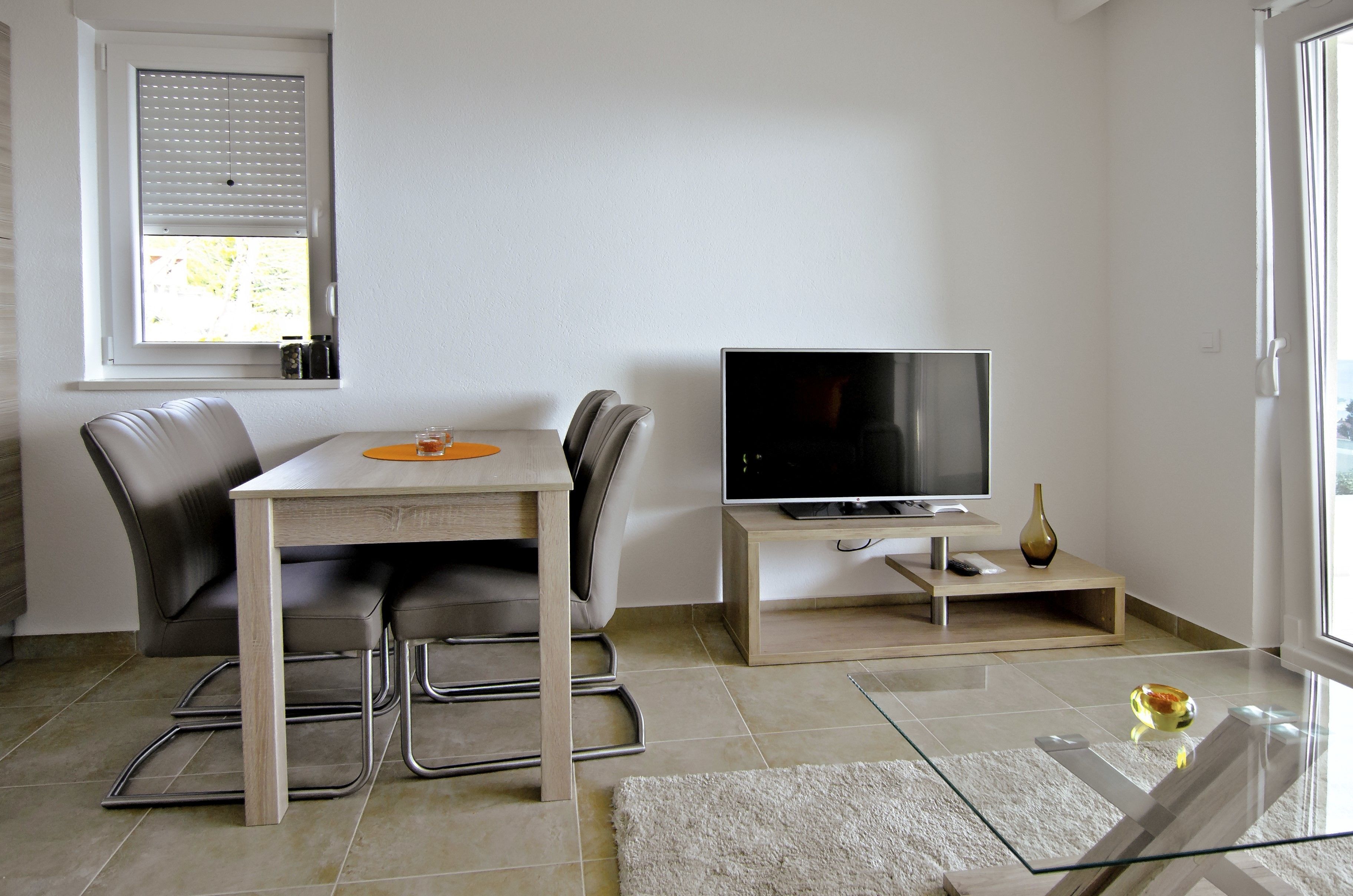 Una sala de estar moderna con una mesa de comedor, sillas, un televisor de pantalla plana y una mesa de centro de vidrio.