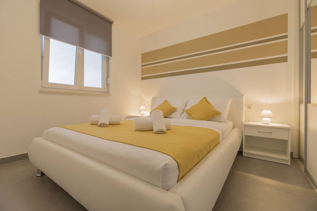 Une chambre d’hôtel moderne avec un grand lit, des tables de chevet avec des lampes et une fenêtre équipée de stores.