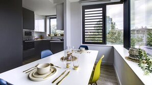 A modern kitchen with dark cabinets, a built-in oven, and a dining area with a white table set for four. - Yugo Explore - Ardcairn House (Dublin)