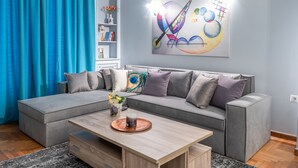 A modern living room with a grey sectional sofa, a wooden coffee table, and a vibrant abstract painting on the wall. - Elite Gem in the heart of Kolonaki (Athens)