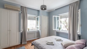 A bedroom with a bed, a wardrobe, and two windows with curtains. - Elite Gem in the heart of Kolonaki (Athens)