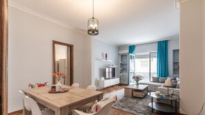 A modern living room with a dining area, a sofa set, a TV, and a balcony with blue curtains. - Elite Gem in the heart of Kolonaki (Athens)