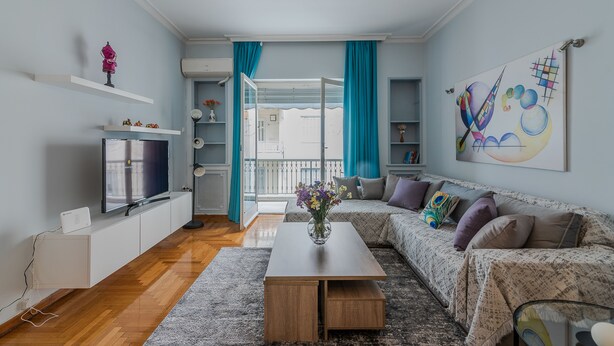 A modern living room with a flat-screen TV, a coffee table with a vase, a sofa with cushions, and a large abstract painting on the wall. - Elite Gem in the heart of Kolonaki (Athens)
