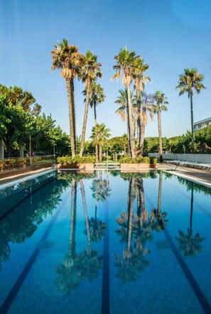 A clear swimming pool surrounded by palm trees, with a clear sky above. - Hostal Bellsol (Pineda de Mar)