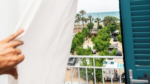 A balcony with a view of a beach, palm trees, and parked cars. - Hostal Bellsol (Pineda de Mar)