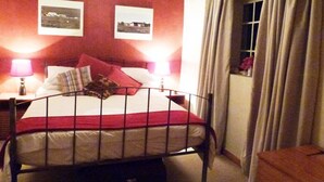 A bedroom with a metal bed frame, two bedside lamps, a window with curtains, and two framed pictures on the wall. - Cosy 6 Person Cottage With Mountain View (Barrydale)