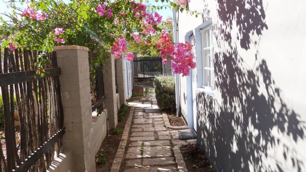 A narrow stone pathway flanked by white walls and a black metal fence, leading to a gate. - Cosy 6 Person Cottage With Mountain View (Barrydale)