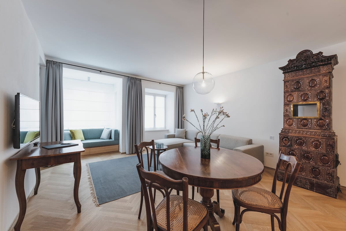 A modern living room with a round wooden dining table, two chairs, a sofa, and a television.