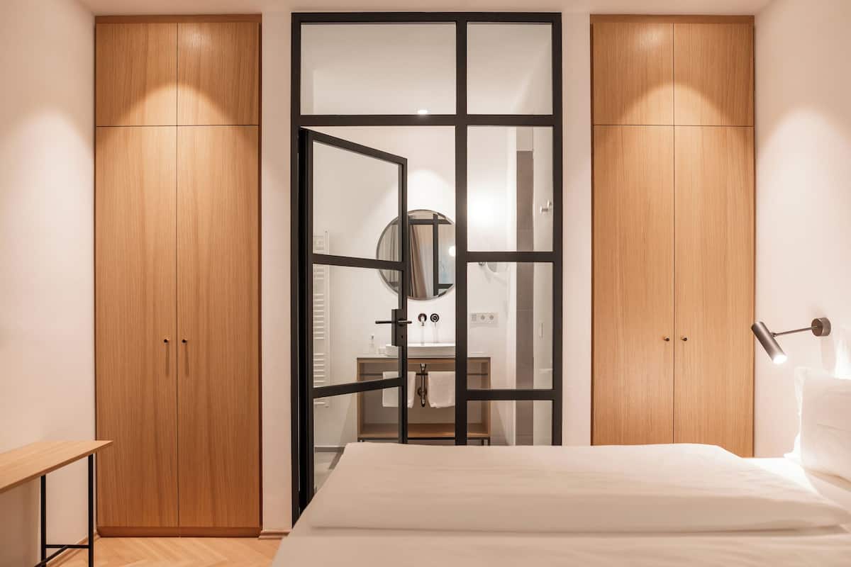 A bedroom with a bed, a wooden wardrobe, and a mirror.