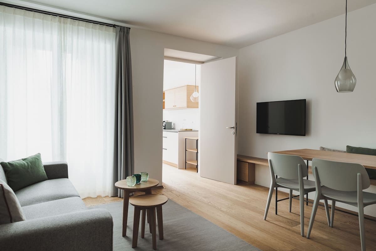 A modern living room with a sofa, a small round table, and a dining area with chairs.