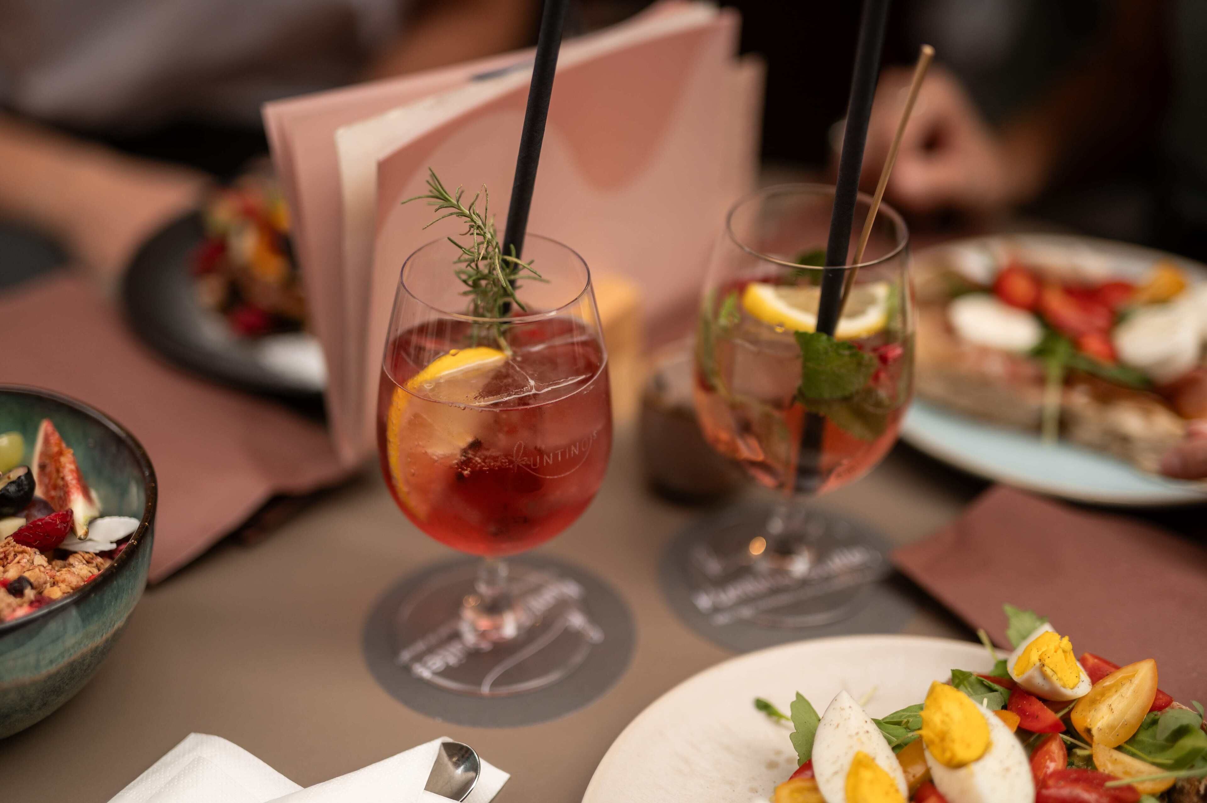 Une table à manger avec deux verres d’une boisson rouge, un bol de granola et une assiette de salade.