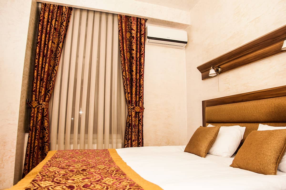 A hotel room with a bed, curtains, an air conditioning unit, and a wooden headboard.
