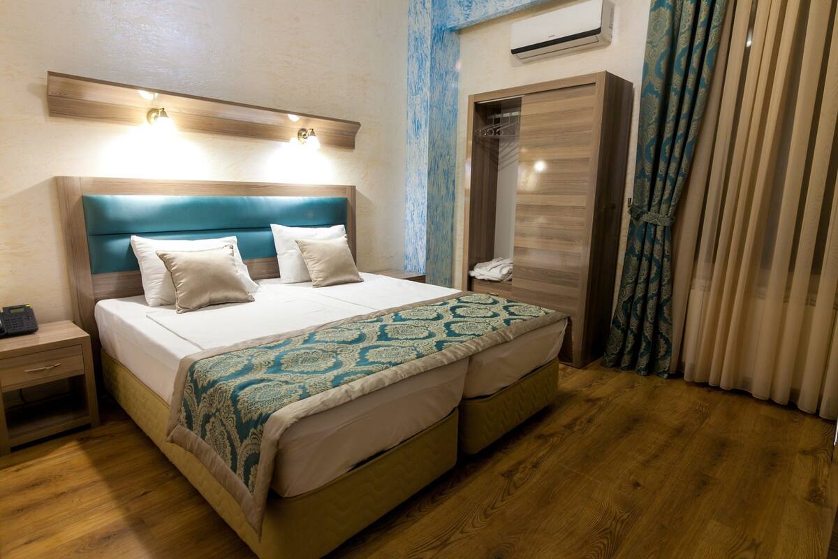 A hotel room with a bed, bedside table, wardrobe, and an air conditioning unit.