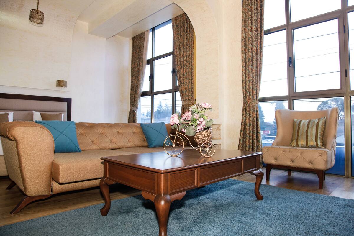 A living room with a sofa, armchair, coffee table, and large windows.