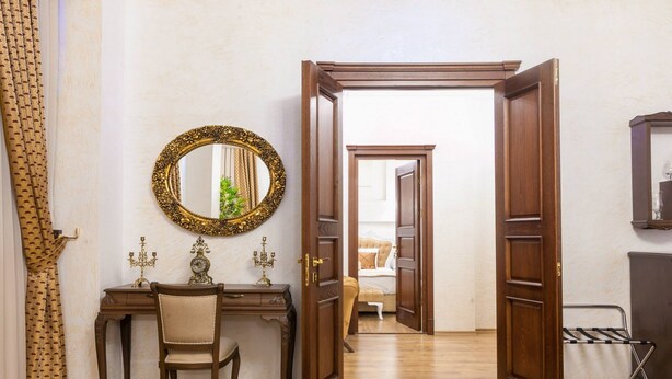 Una habitación con un escritorio de madera, una silla, un espejo y una puerta que da a otra habitación.
