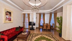 Una sala de estar con un sofá rojo, una mesa de centro, un televisor, una zona de comedor con sillas y una planta grande.