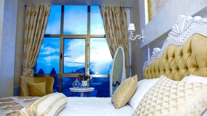 Un dormitorio con una cama grande, una ventana con cortinas, una mesita de noche con flores y un espejo.