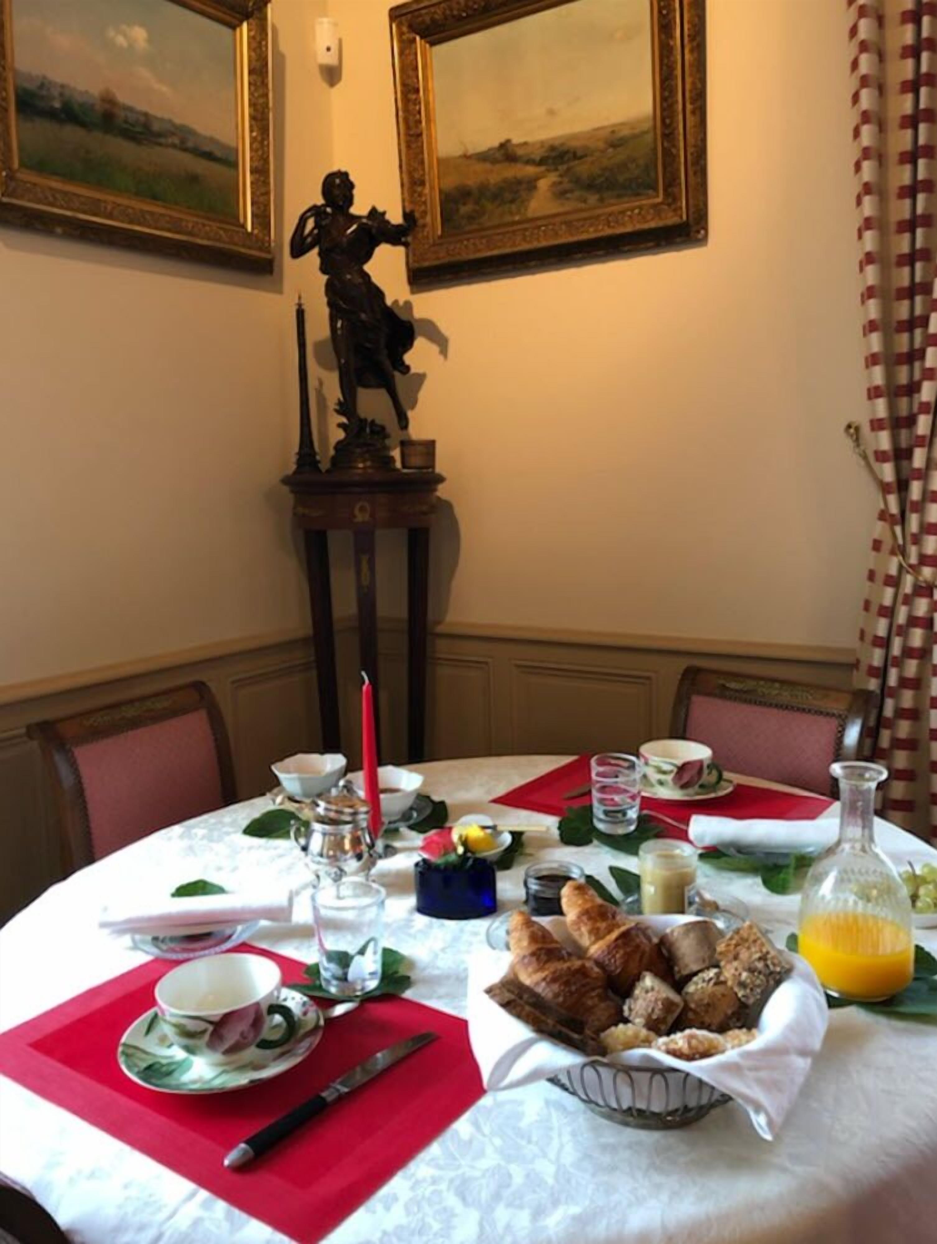 Een eettafel gedekt met ontbijtartikelen, een beeld en lijstjes met schilderijen aan de muur.