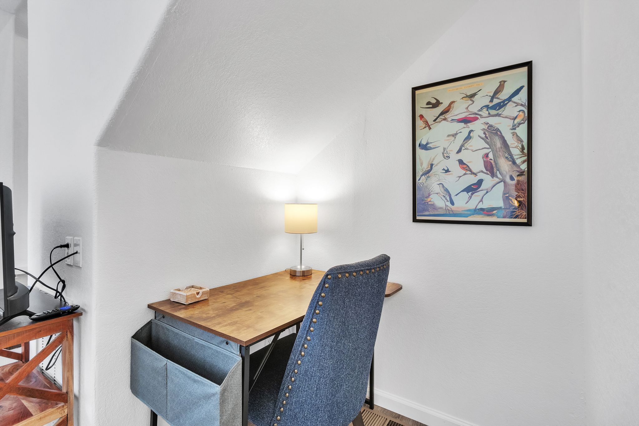 A room with a wooden table, a lamp, a chair, and a wall-mounted picture.