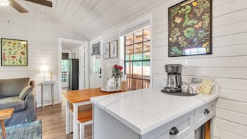 A modern kitchen with white cabinetry, a marble countertop, and a coffee maker.