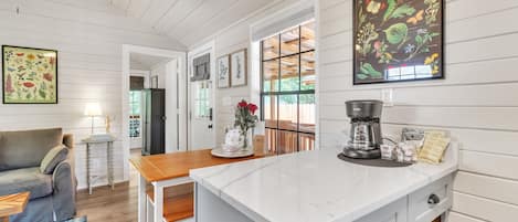 A modern kitchen with white cabinetry, a marble countertop, and a coffee maker.