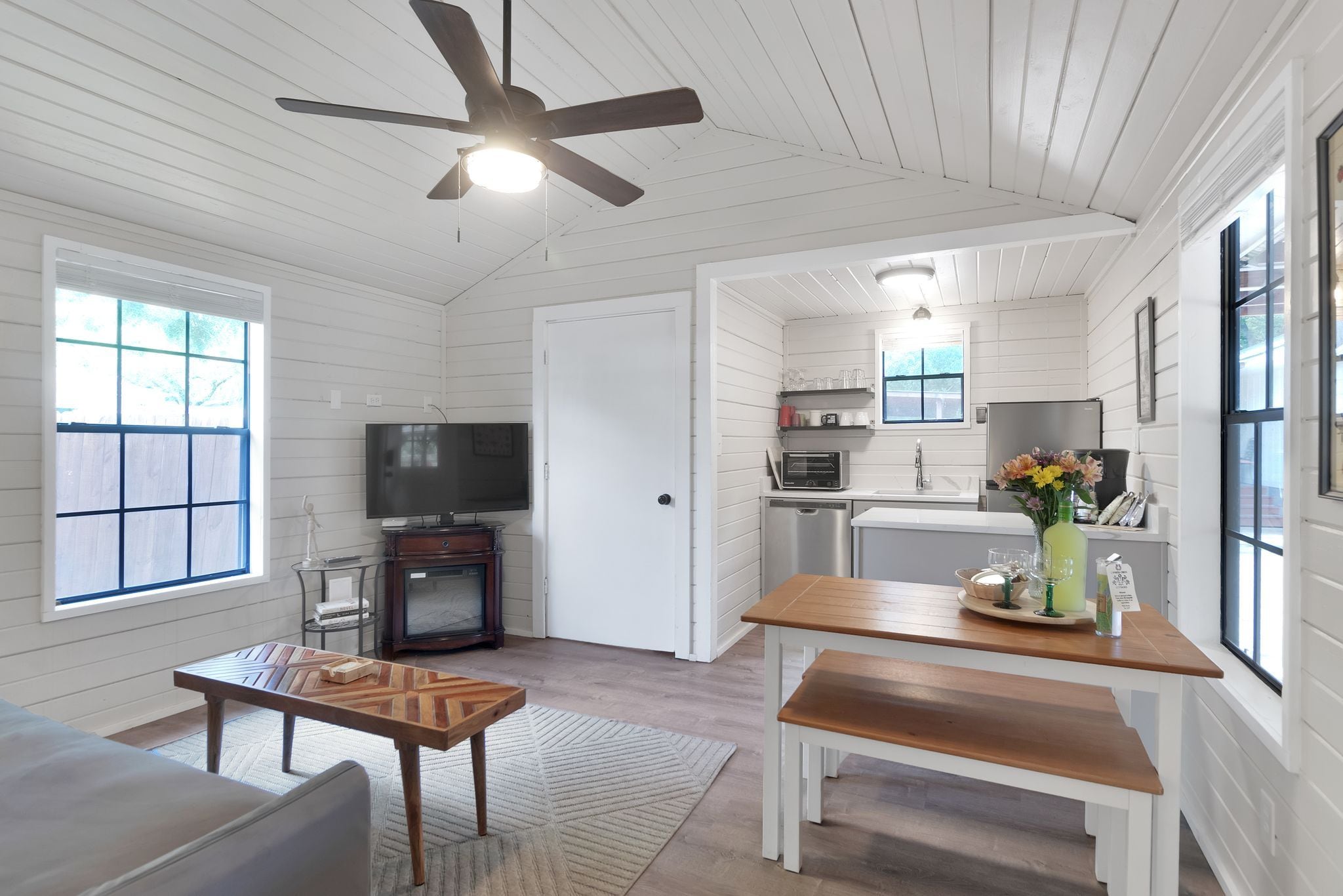 A spacious living area with a television, seating, a ceiling fan, and a kitchen with a sink and countertop.