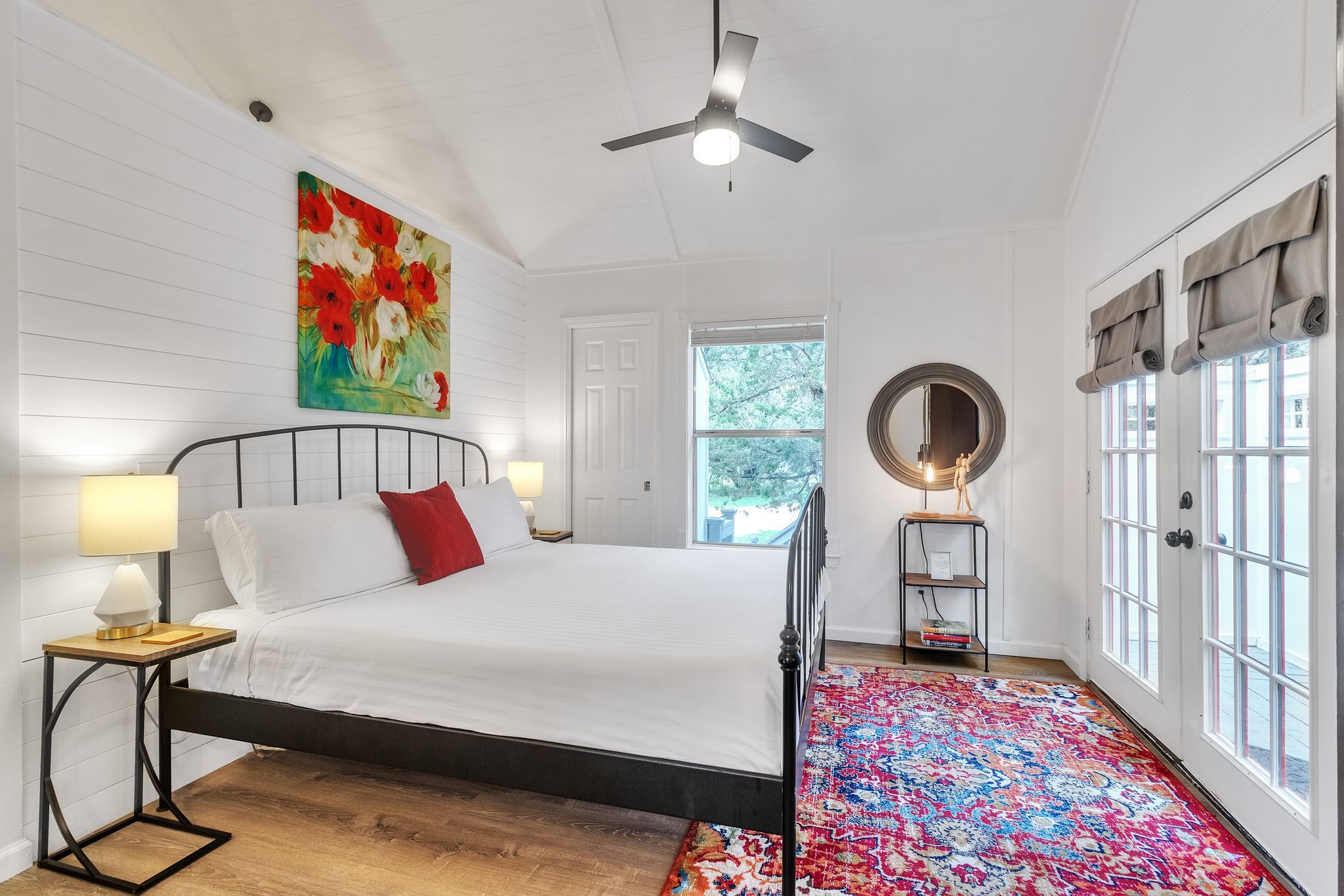 Un dormitorio con cama, mesita de noche, lámpara de pie, ventilador de techo, ventana grande y puerta.