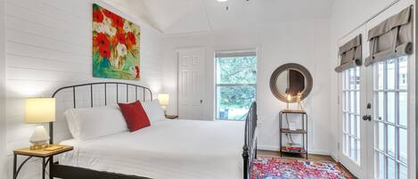 Un dormitorio con cama, mesita de noche, lámpara de pie, ventilador de techo, ventana grande y puerta.