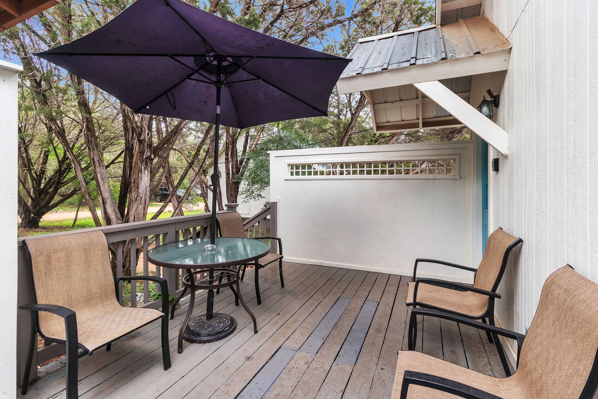 Une terrasse extérieure avec une table ronde et des chaises, un parasol violet et une clôture blanche.