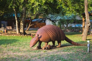 Eine große Bronzestatue eines Nashorns in einer grünen Landschaft mit Bäumen und einer Schaukel im Hintergrund.