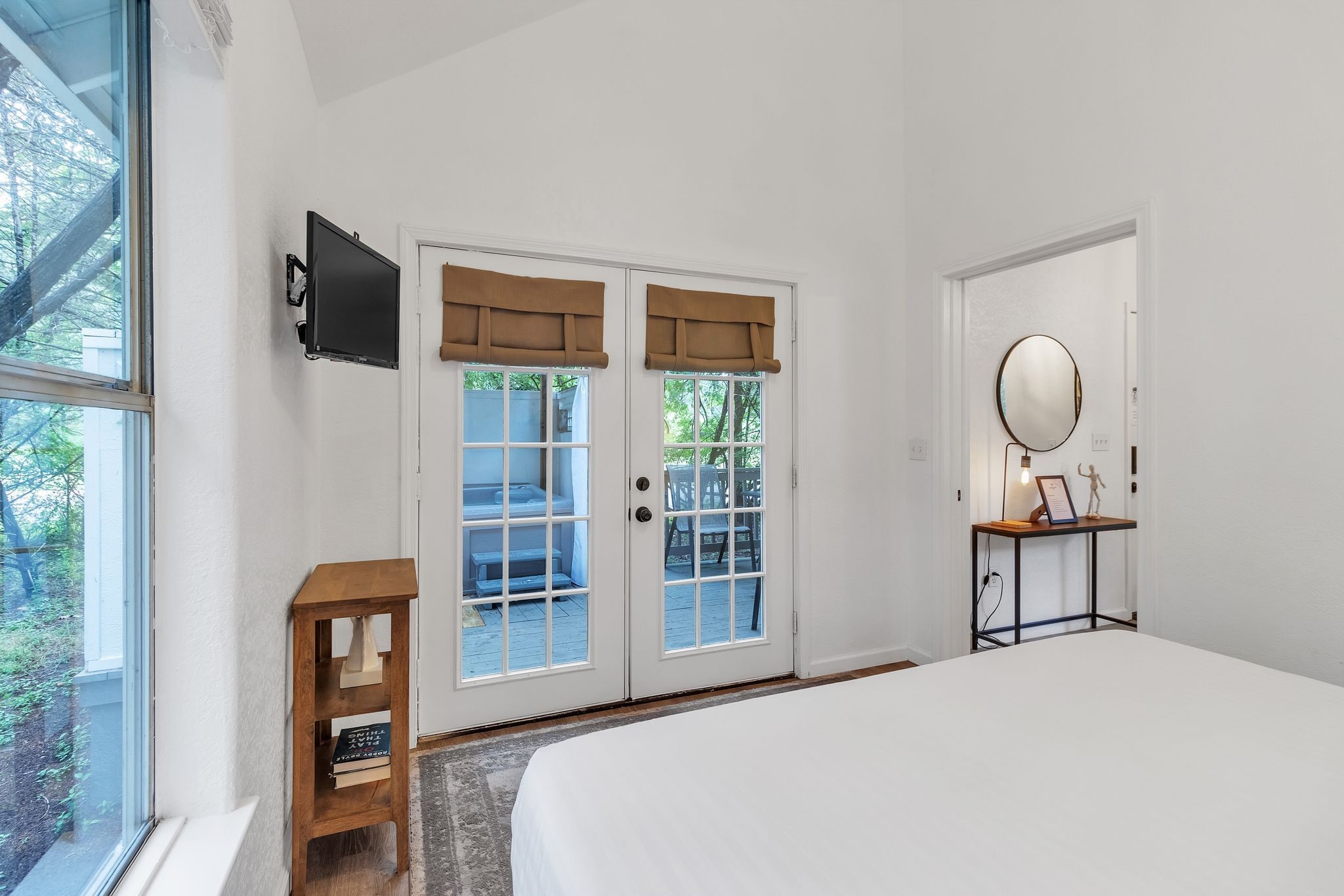 A bedroom with a large bed, a bedside table with a lamp, a TV mounted on the wall, and a door with a view to the outside.