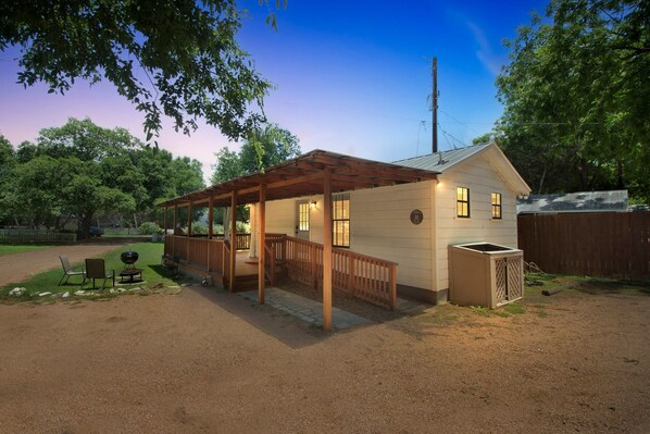 Ein Bungalow mit überdachter Veranda, umzäunter Garten und einer kleinen Sitzgelegenheit im Freien.
