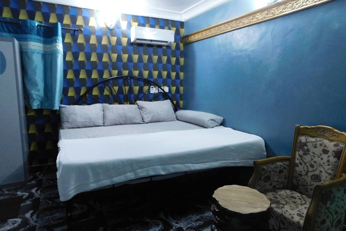 A bedroom with a bed, a chair, a small table, and a patterned wall.