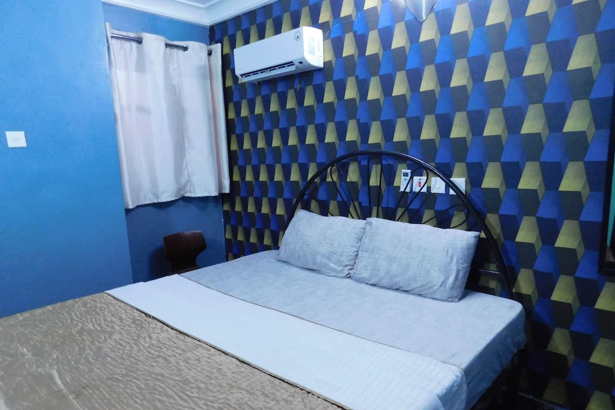 A room with a bed, a chair, and an air conditioning unit on the wall.