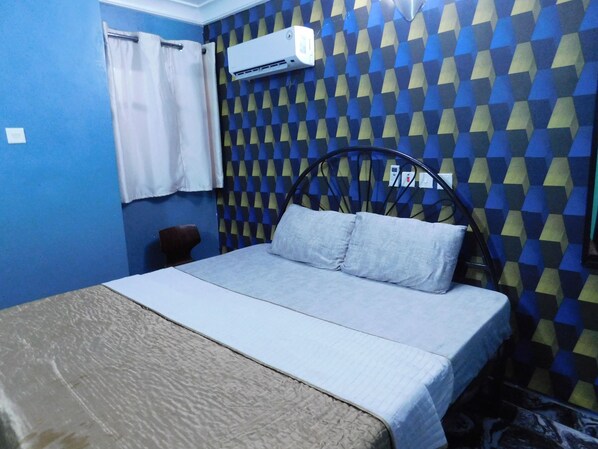 A room with a bed, a chair, and an air conditioning unit on the wall.