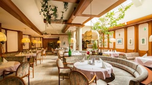 A restaurant with round tables, cushioned seating, hanging plants, and framed pictures on the walls. - Hotel Restaurant Kollar Göbl (Deutschlandsberg)