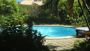 Ein Swimmingpool, umgeben von üppigem Grün und mit freiem Blick auf den Ozean.