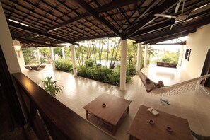 Un'area salotto all'aperto coperta con tavoli e panche in legno, un'amaca e vista sulla piscina e sul verde.