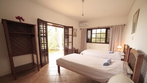 Ein Hotelzimmer mit zwei Betten, einer hölzernen Bank, einer Klimaanlage und Blick ins Freie.