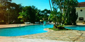 Une piscine dotée d’une terrasse carrelée, entourée de palmiers et de chaises longues.
