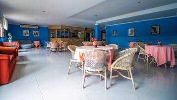Un grand espace dédié à la salle à manger, avec des chaises et des tables en osier, un coin bar et des murs bleus ornés de tableaux encadrés.