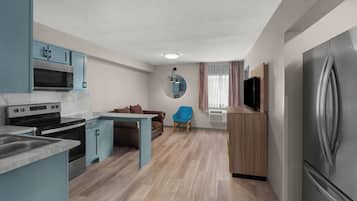 Cocina compacta con microondas, estufa y refrigerador, una silla azul y una pequeña mesa de comedor.