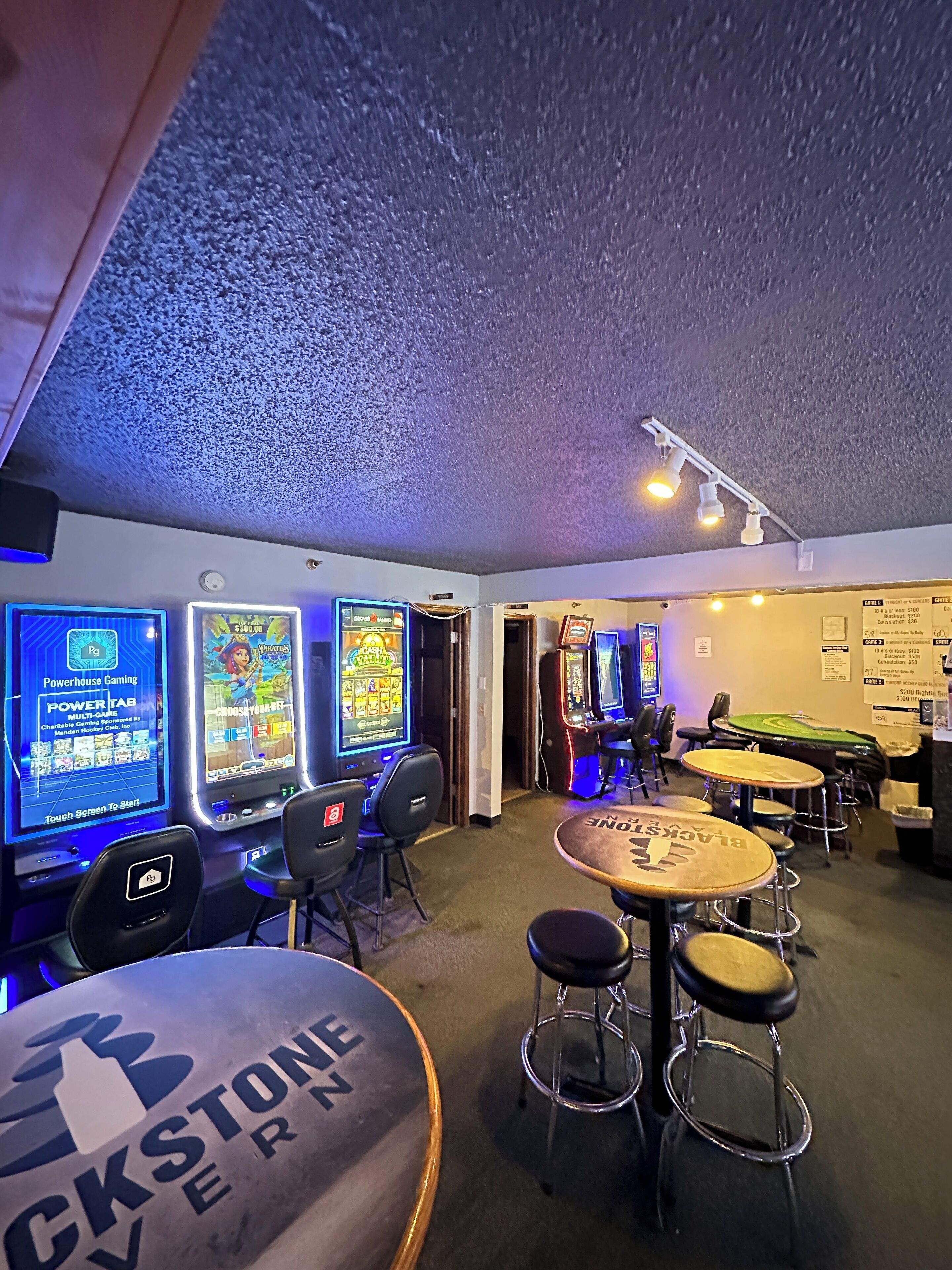 A gaming area with multiple slot machines, a pool table, and bar stools.