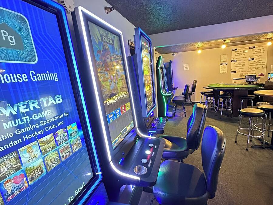 Zona de juegos con varias máquinas recreativas, sillas y una barra.