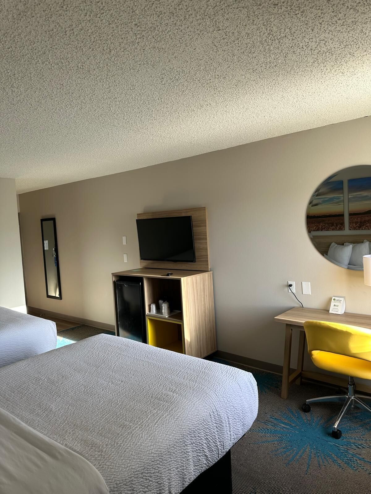 A hotel room with two beds, a desk, a TV, and a view of the outdoors.
