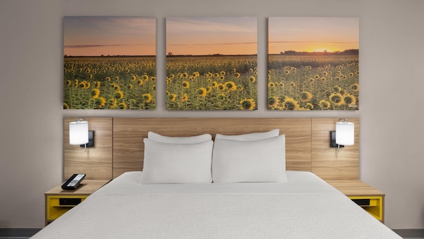 A hotel room with a large bed, two bedside tables with lamps, and a wall-mounted artwork of a sunflower field. - Days Inn by Wyndham Mandan Bismarck Area (Mandan)