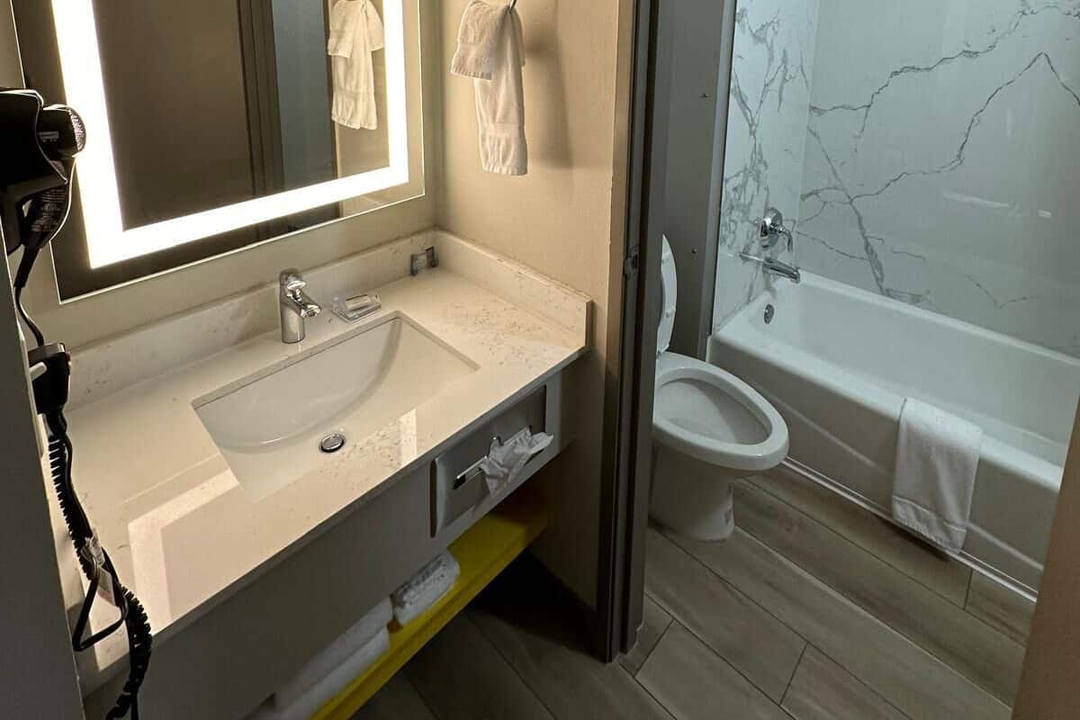 A modern bathroom with a large mirror, a sink, a toilet, and a shower.