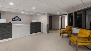 A reception area with a Days Inn sign, a reception desk, a laptop, a trash can, and yellow chairs. - Days Inn by Wyndham Mandan Bismarck Area (Mandan)