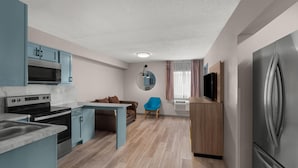 A modern kitchen with built-in appliances, a dining area with a blue chair, and a small seating area with a brown sofa. - Days Inn by Wyndham Mandan Bismarck Area (Mandan)