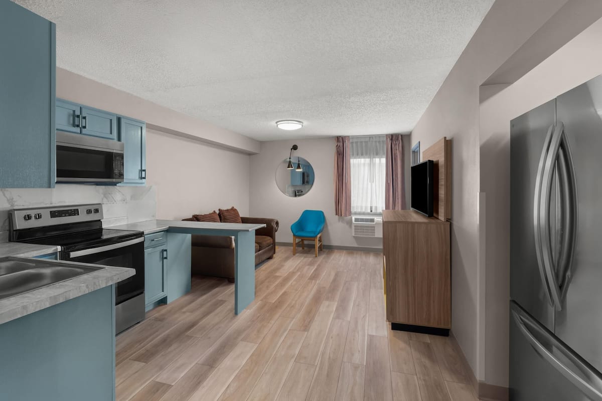 A modern kitchen with built-in appliances, a dining area with a blue chair, and a small seating area with a brown sofa.